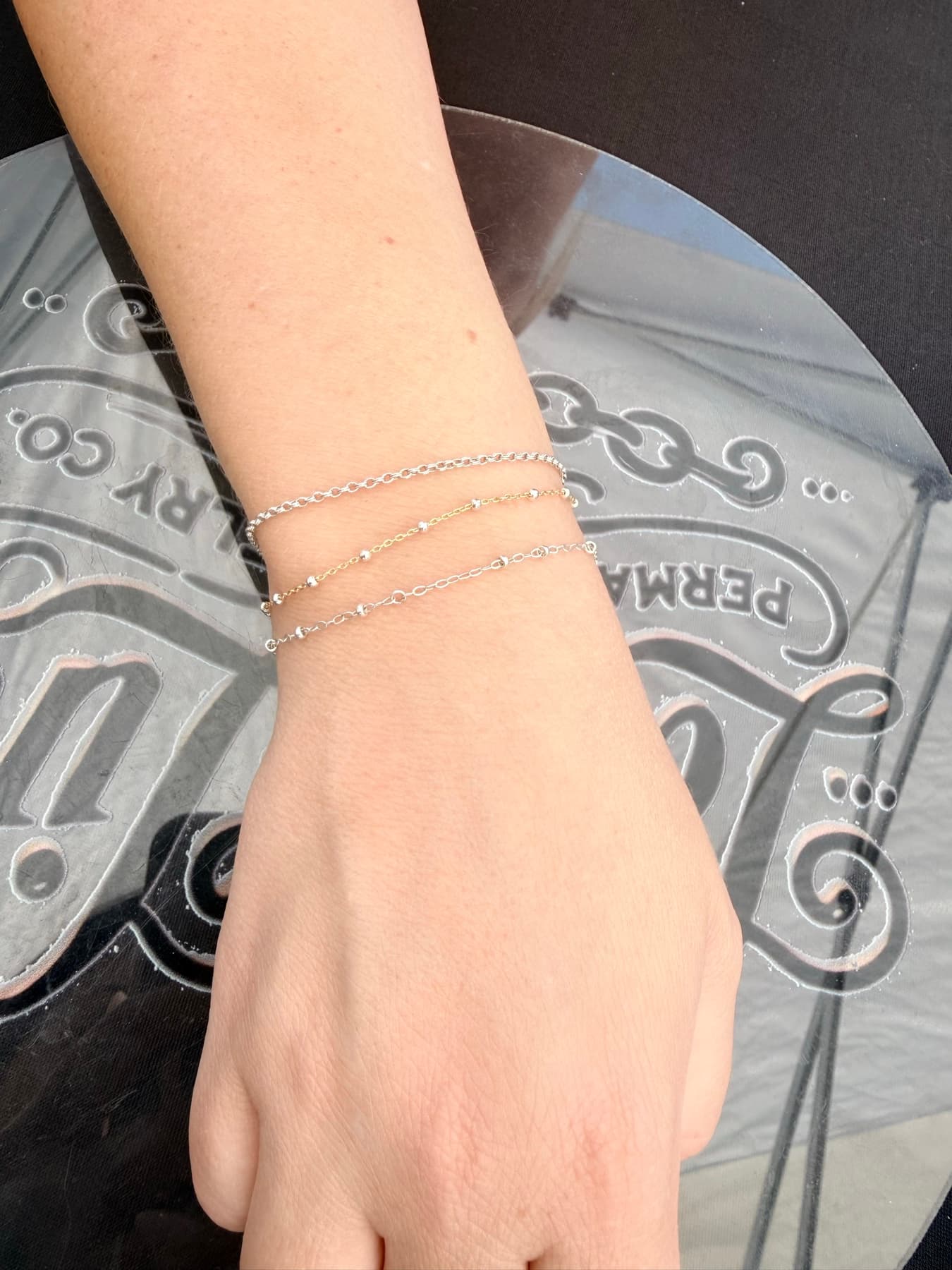 Three fine permanent bracelets on a wrist resting on the Lady Link logo